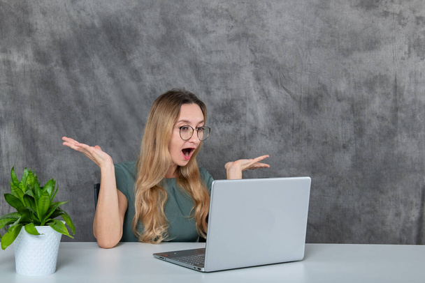 One girl with glasses and a flower looks at the laptop in surprise. High quality photo - Foto, afbeelding