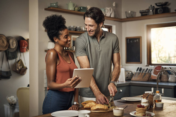 Interracial couple, tablet and cooking in kitchen for recipe, social media or online food vlog at home. Man and woman preparing breakfast meal or cutting ingredients together with technology on table. - Foto, Bild