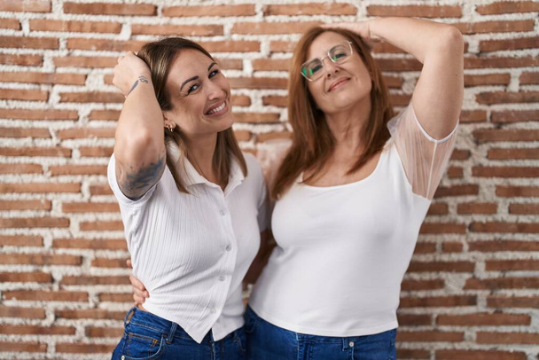 Mãe e filha hispânica vestindo casual t-shirt branca sorrindo confiante tocando o cabelo com mão para cima gesto, posando atraente e elegante  - Foto, Imagem