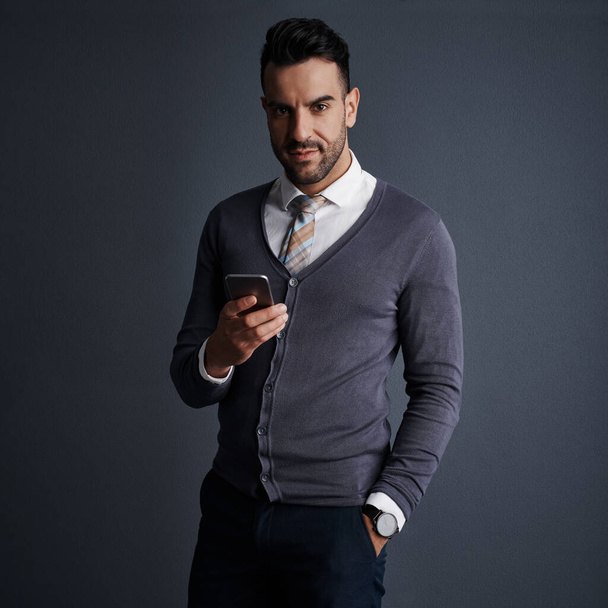 Availability is the key to my success. Studio shot of a stylish young businessman using a mobile phone against a gray background - Fotoğraf, Görsel