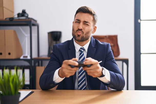 Handsome hispanic man playing video games at the office looking at the camera blowing a kiss being lovely and sexy. love expression.  - Foto, Bild