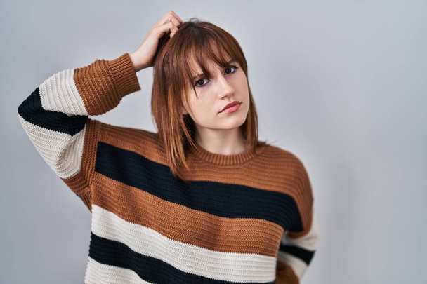 Young beautiful woman wearing striped sweater over isolated background confuse and wondering about question. uncertain with doubt, thinking with hand on head. pensive concept.  - Foto, afbeelding