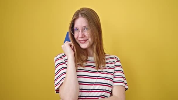 Jovem loira sorrindo confiante segurando cartão de crédito sobre fundo amarelo isolado - Filmagem, Vídeo