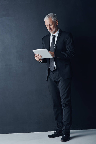 Increased accessibility means increased productivity. Studio shot of a mature businessman using a digital tablet against a dark background - Foto, Imagen