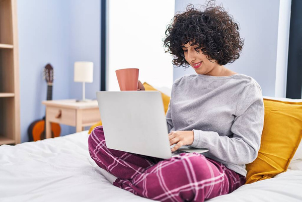 Young middle east woman using laptop drinking coffee sitting on bed at bedroom - Foto, Bild
