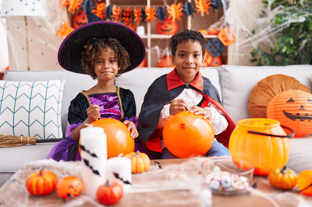 Adorable afroamericano chico y chica teniendo halloween fiesta dibujo en globo en casa - Foto, imagen