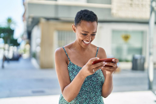 Afrikkalainen amerikkalainen nainen hymyilee luottavainen katsomassa videota älypuhelimella kadulla - Valokuva, kuva