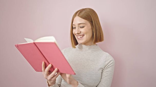fiatal szőke nő mosolygós magabiztos olvasmány könyv felett elszigetelt rózsaszín háttér - Fotó, kép