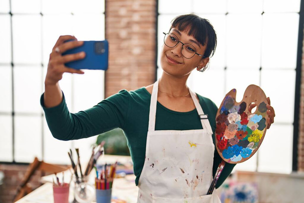 Молода красива іспаномовна жінка художник посміхається впевнено зробити селфі за допомогою смартфона в художній студії
 - Фото, зображення