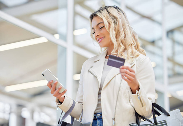Credit card, phone and a woman doing online shopping at a mall for retail sale and discount. Happy, ecommerce and a girl with easy pay on a mobile app while in a shop for a deal, payment or bag. - Photo, Image