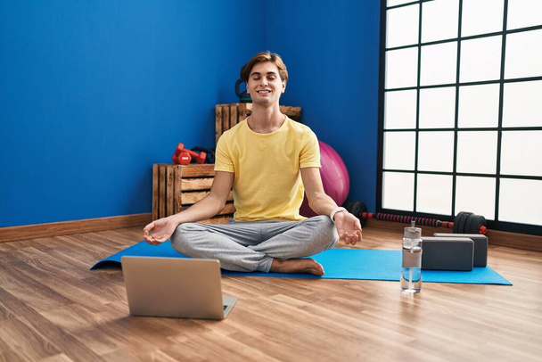 Young caucasian man smiling confident having online yoga class at sport center - Photo, Image