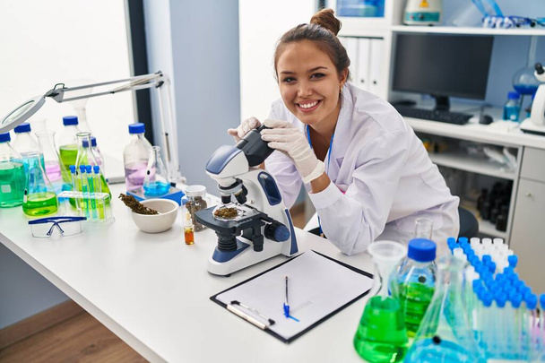 Young beautiful hispanic woman scientist smiling confident using microscope at laboratory - Zdjęcie, obraz