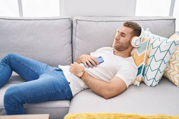 Young caucasian man listening to music lying on sofa at home - Photo, image