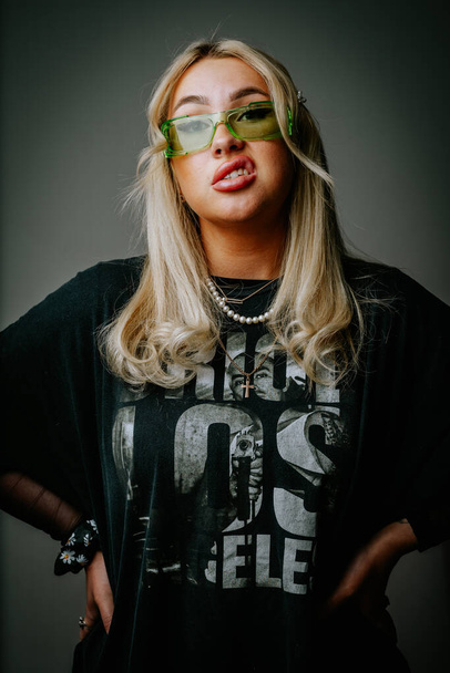 A blonde girl in green glasses and dark clothes is photographed in the studio on a dark background - Valokuva, kuva
