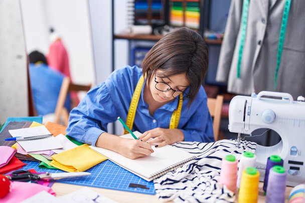 Чарівний іспаномовний дівчина кравець малюнок на ноутбуці на фабриці одягу
 - Фото, зображення