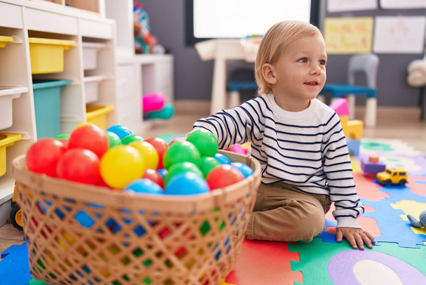 Adorable chico caucásico jugando con bolas sentadas en el suelo en el jardín de infantes - Foto, Imagen