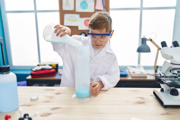 Entzückende hispanische Junge Student lächelt zuversichtlich Gießen Flüssigkeit auf Reagenzglas im Labor Klassenzimmer - Foto, Bild