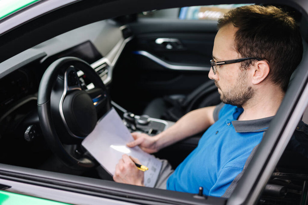 車の検査中に男性の機械工の側面図は文書を記入します。男は車の中に座っている。高品質の写真 - 写真・画像