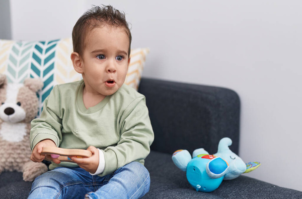 Adorable hispanic boy playing with toy sitting on sofa at home - Photo, Image