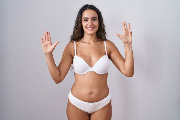 Mujer hispana joven vistiendo lencería blanca mostrando y señalando con los dedos el número nueve mientras sonríe confiada y feliz.  - Foto, Imagen