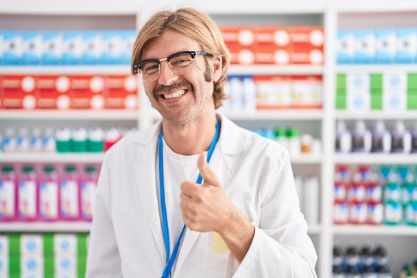Καυκάσιος με μουστάκι που δουλεύει στο φαρμακείο και κάνει χαρούμενες χειρονομίες με το χέρι. έγκριση έκφρασης κοιτάζοντας την κάμερα που δείχνει την επιτυχία.  - Φωτογραφία, εικόνα