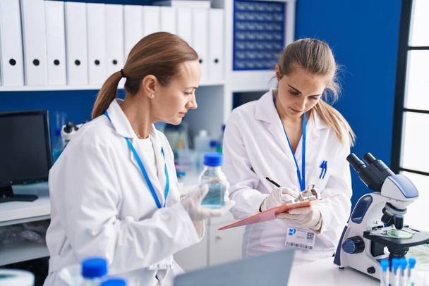 Two women scientists write on document measuring liquid at laboratory - Fotoğraf, Görsel