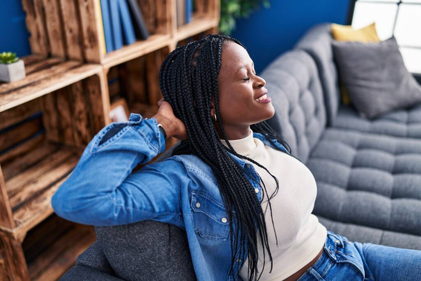 Afro-Amerikaanse vrouw ontspannen met handen op het hoofd zitten op de bank thuis - Foto, afbeelding