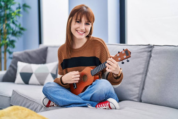 Молодая женщина играет ukelele сидя дома на диване - Фото, изображение