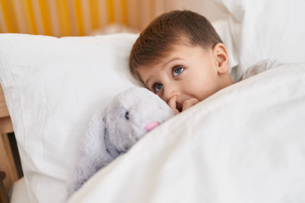 Αξιολάτρευτο καυκάσιο αγόρι ξαπλωμένο στο κρεβάτι με κούκλα στο υπνοδωμάτιο - Φωτογραφία, εικόνα
