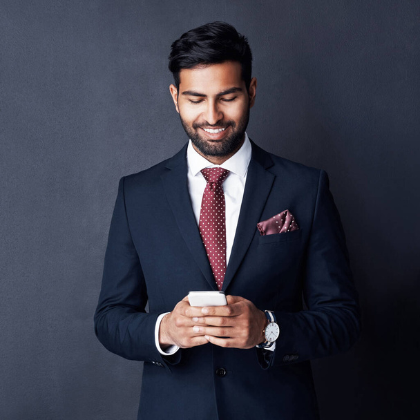 Keeping his career on track by staying connected. Studio shot of a young businessman using a mobile phone against a gray background - Foto, Bild