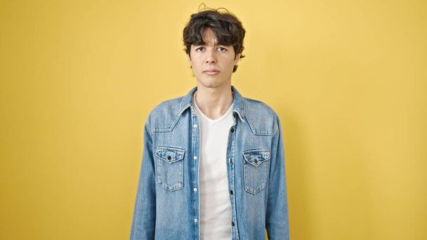 Junger hispanischer Mann steht mit ernstem Gesichtsausdruck vor isoliertem gelben Hintergrund - Foto, Bild