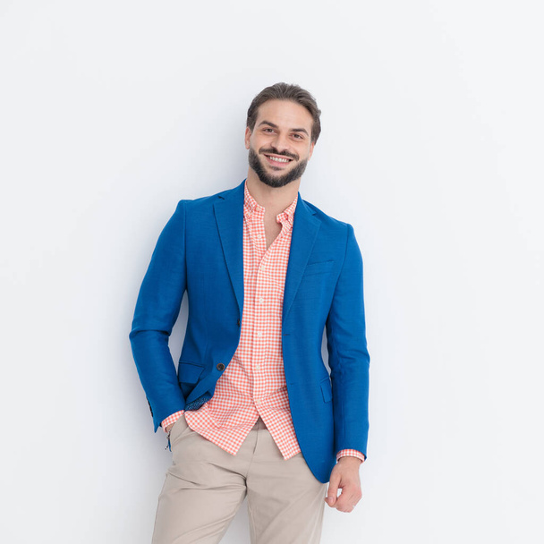 muotokuva onnellinen älykäs rento mies yllään sininen takki kädestä taskussa ja hymyillen poseeratessaan edessä vaaleanharmaa tausta - Valokuva, kuva