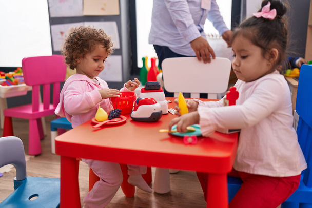 Adorable girls playing supermarket game sitting on table at kindergarten - Zdjęcie, obraz