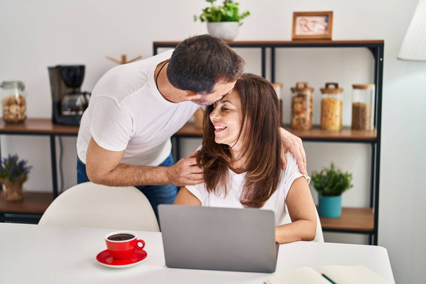 Middle age man and woman couple hugging each other working sitting on table at home - Photo, Image