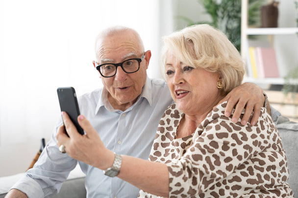 Elderly couple using phone and having video call. Mature wife and husband talking on telephone - Fotoğraf, Görsel