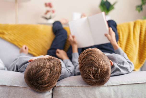 Uroczy chłopcy czytają książki leżące na kanapie w domu - Zdjęcie, obraz