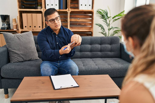 Joven psicólogo latino teniendo sesión mental sosteniendo cerebro en clínica de psicología - Foto, imagen