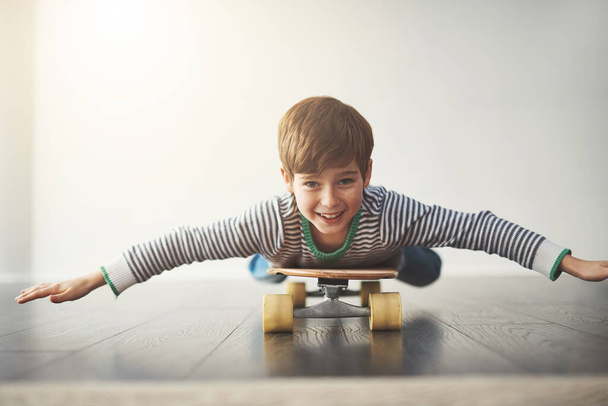 Пытаюсь найти баланс. Портрет веселого маленького мальчика, лежащего дома на скейтборде в течение дня - Фото, изображение