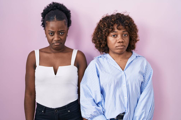 Duas mulheres africanas em pé sobre fundo rosa cético e nervoso, franzindo a testa chateado por causa do problema. pessoa negativa.  - Foto, Imagem