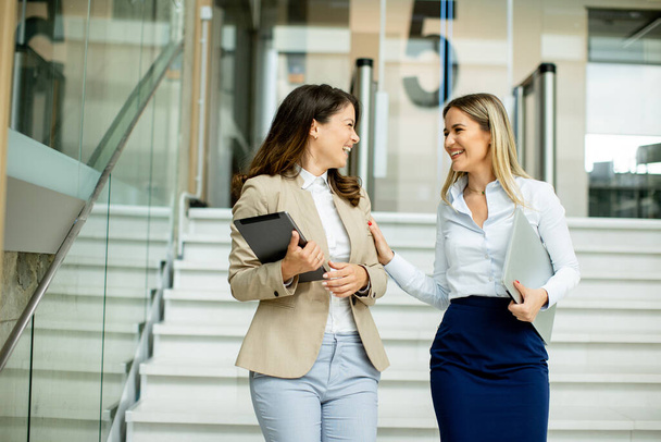 Two cute young business women walking on stairs in the office hallway - Fotoğraf, Görsel