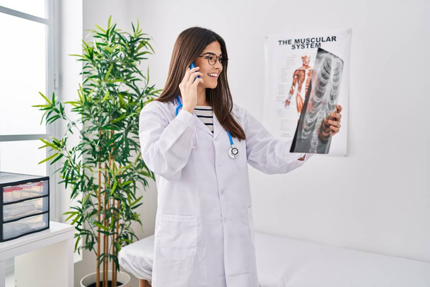 Młoda piękna Latynoska lekarz rozmawia na smartfonie z Xray w klinice - Zdjęcie, obraz
