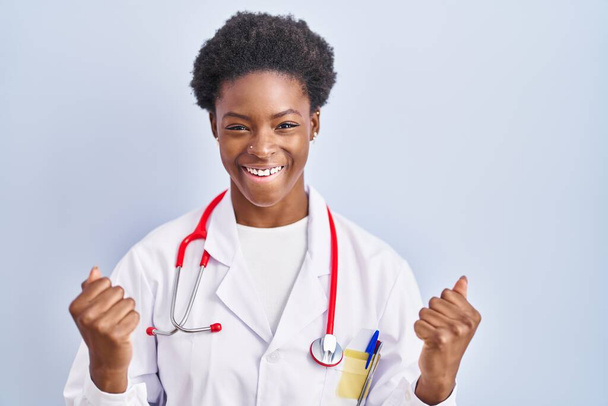 Afrikkalainen amerikkalainen nainen yllään lääkäri univormu ja stetoskooppi huutaa ylpeä, juhlii voittoa ja menestystä hyvin innoissaan nosti kädet  - Valokuva, kuva