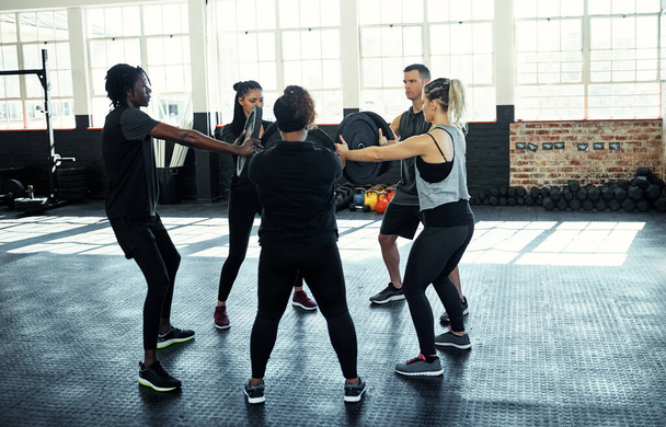 A suar no ginásio. um grupo de fitness usando placas de peso em sua sessão no ginásio - Foto, Imagem