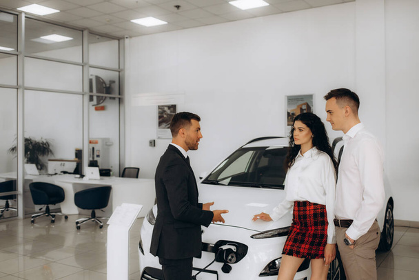 gerente de venta de coches eléctricos a una pareja joven en un concesionario de coches. - Foto, imagen