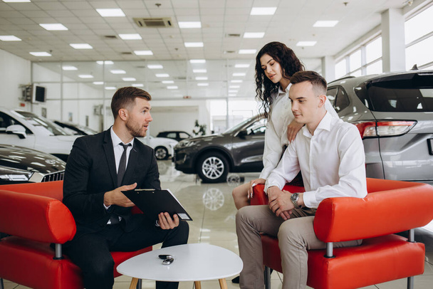 Взрослая пара беседует с агентом по продажам и подписывает контракт на новый автомобиль в салоне современных автомобилей - Фото, изображение