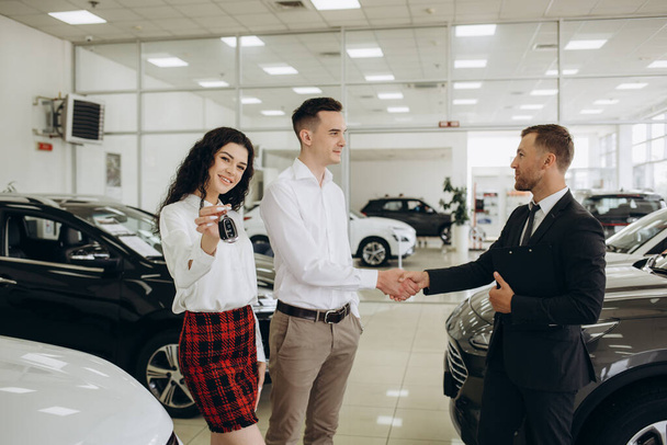 Car dealer showing car to couple in showroom. - Photo, Image