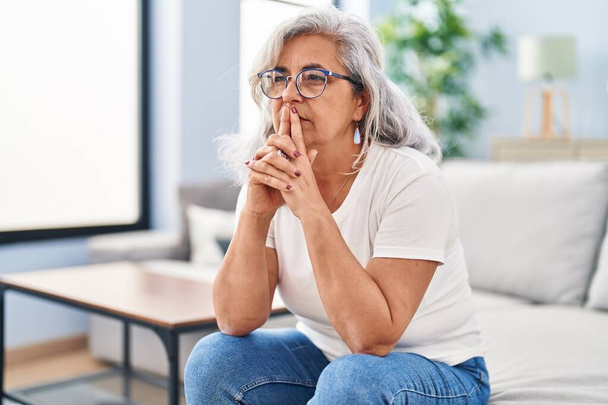 Frau mittleren Alters sitzt gestresst zu Hause auf dem Sofa - Foto, Bild