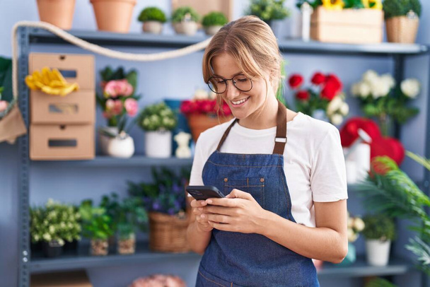 Young blonde girl florist smiling confident using smartphone at florist - Photo, Image