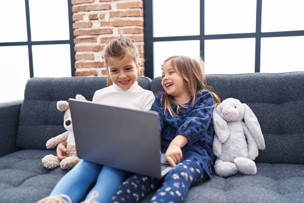 Schattige meisjes met behulp van laptop zitten op de bank thuis - Foto, afbeelding