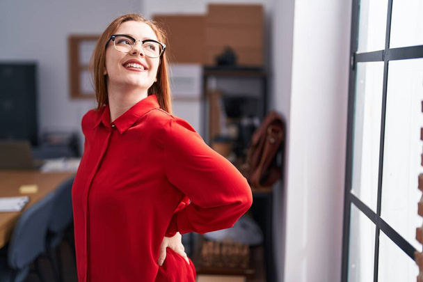 若い赤毛の女性実業家はオフィスで自信を持って笑っている - 写真・画像
